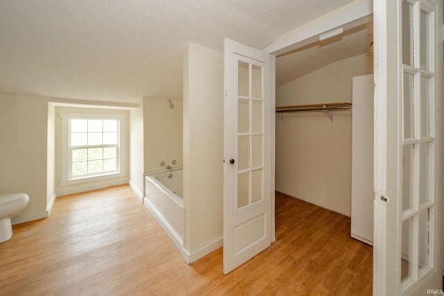 bathroom with vaulted ceiling, wood finished floors, tub / shower combination, french doors, and toilet