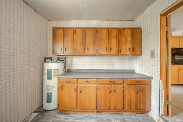 kitchen featuring water heater, black oven, brown cabinetry, and wallpapered walls