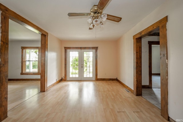 spare room featuring french doors, light wood-style floors, a ceiling fan, and baseboards