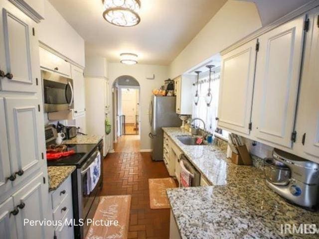 1700 W Taylor St, Kokomo, IN 46901 - kitchen featuring stainless steel appliances, a sink, brick patterned flooring, arched walkways, and light stone countertops