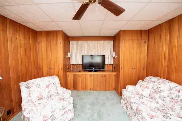 living area with light colored carpet, wooden walls, ceiling fan, and a paneled ceiling