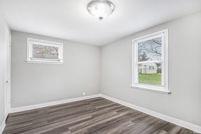 spare room featuring plenty of natural light, dark wood-type flooring, and baseboards