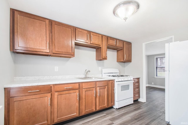 kitchen with white appliances, a sink, light countertops, wood finished floors, and brown cabinetry