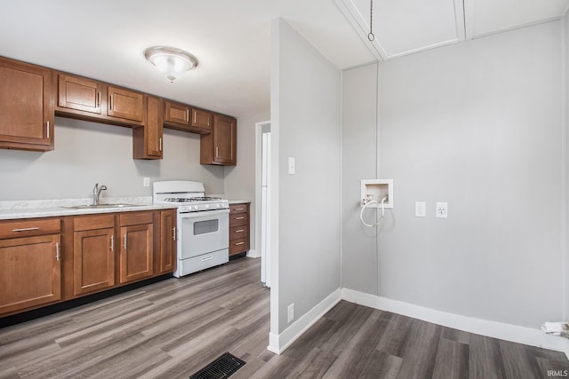 kitchen featuring gas range gas stove, a sink, wood finished floors, light countertops, and brown cabinets