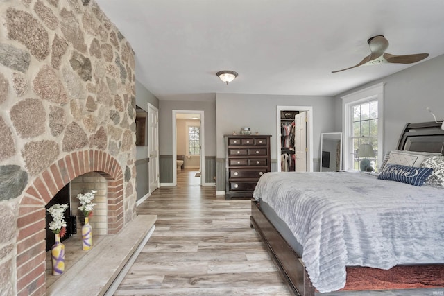 bedroom with light wood-style floors, a spacious closet, a fireplace, a closet, and a ceiling fan