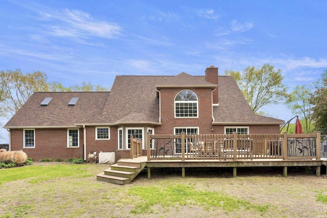back of house featuring brick siding, a chimney, a yard, roof with shingles, and a wooden deck