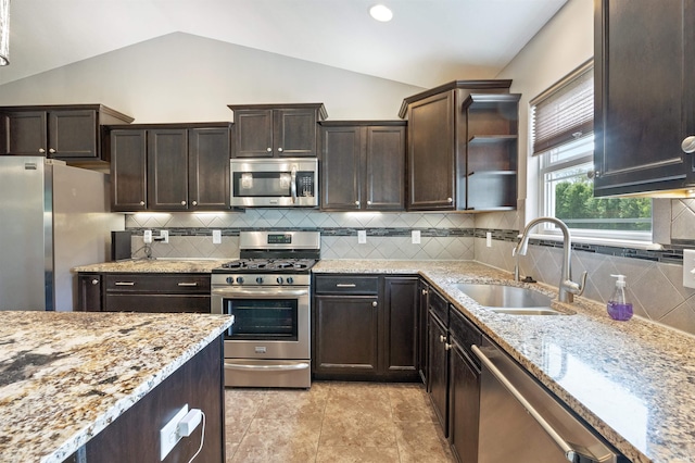 kitchen featuring stainless steel appliances, a sink, lofted ceiling, light stone countertops, and dark brown cabinetry