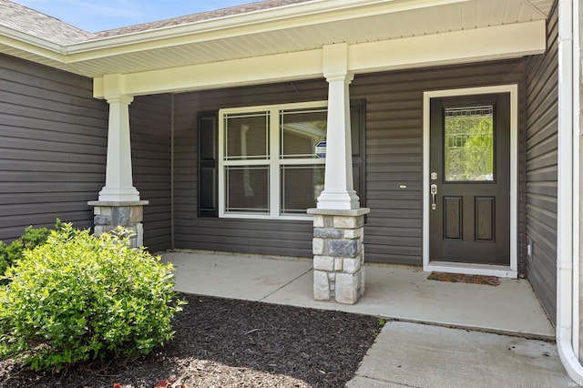 view of exterior entry featuring covered porch and a shingled roof