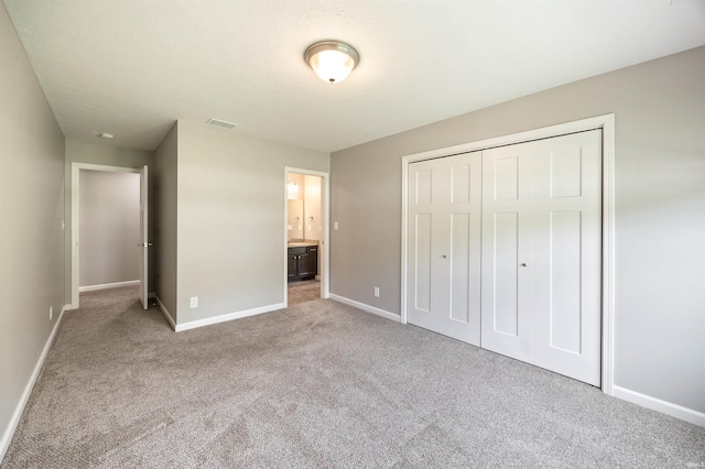 unfurnished bedroom with carpet floors, baseboards, a closet, and ensuite bathroom