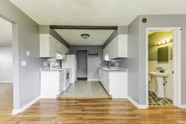 kitchen with electric stove, a textured ceiling, a sink, under cabinet range hood, and light countertops