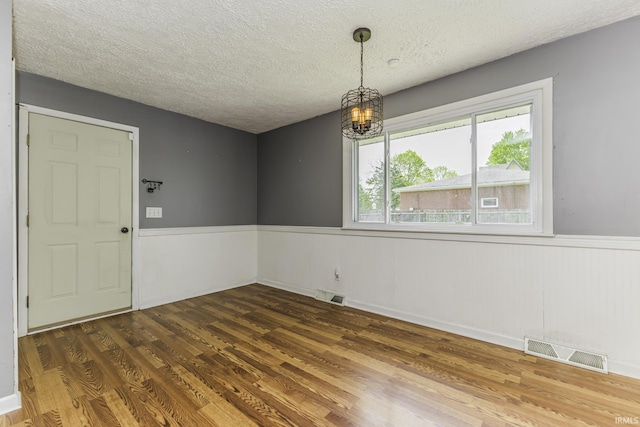 empty room with a chandelier, wainscoting, wood finished floors, and a textured ceiling
