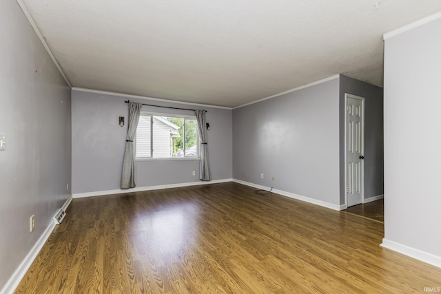 spare room featuring wood finished floors, crown molding, and baseboards