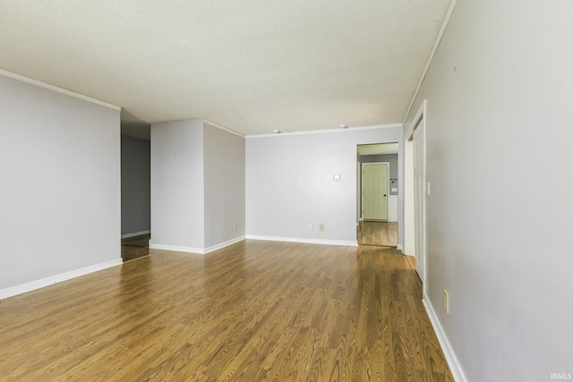 empty room with wood finished floors, baseboards, a textured ceiling, and crown molding