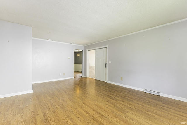 spare room with crown molding, light wood-style floors, baseboards, and a textured ceiling