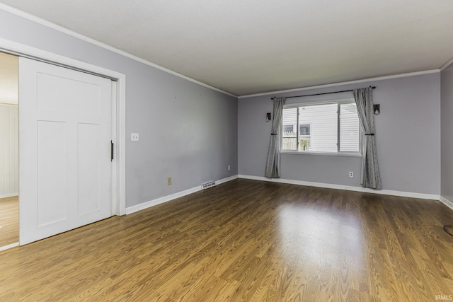 spare room featuring crown molding, wood finished floors, and baseboards
