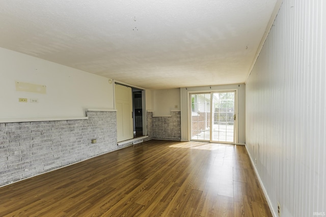 unfurnished living room featuring dark wood-style flooring and brick wall