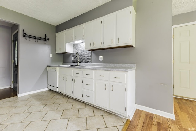 kitchen with a sink, dishwasher, light countertops, white cabinets, and baseboards