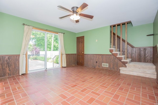 927 S Lombard Ave, Evansville, IN 47714 - unfurnished living room featuring wainscoting, brick patterned flooring, a ceiling fan, stairway, and wood walls