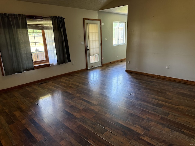 spare room featuring dark wood finished floors, plenty of natural light, vaulted ceiling, and baseboards