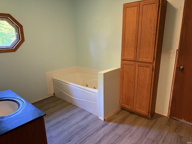 bathroom featuring wood finished floors, a whirlpool tub, baseboards, and vanity