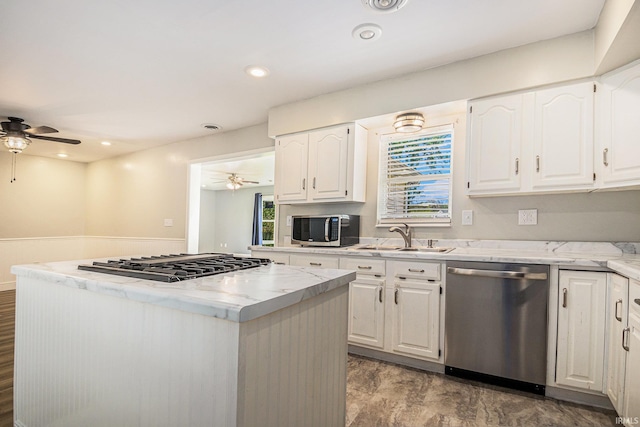 kitchen with stainless steel appliances, ceiling fan, a sink, a center island, and white cabinets