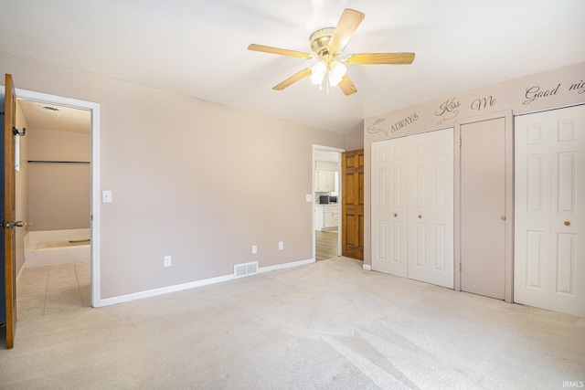 unfurnished bedroom with multiple closets, light colored carpet, ensuite bath, baseboards, and ceiling fan