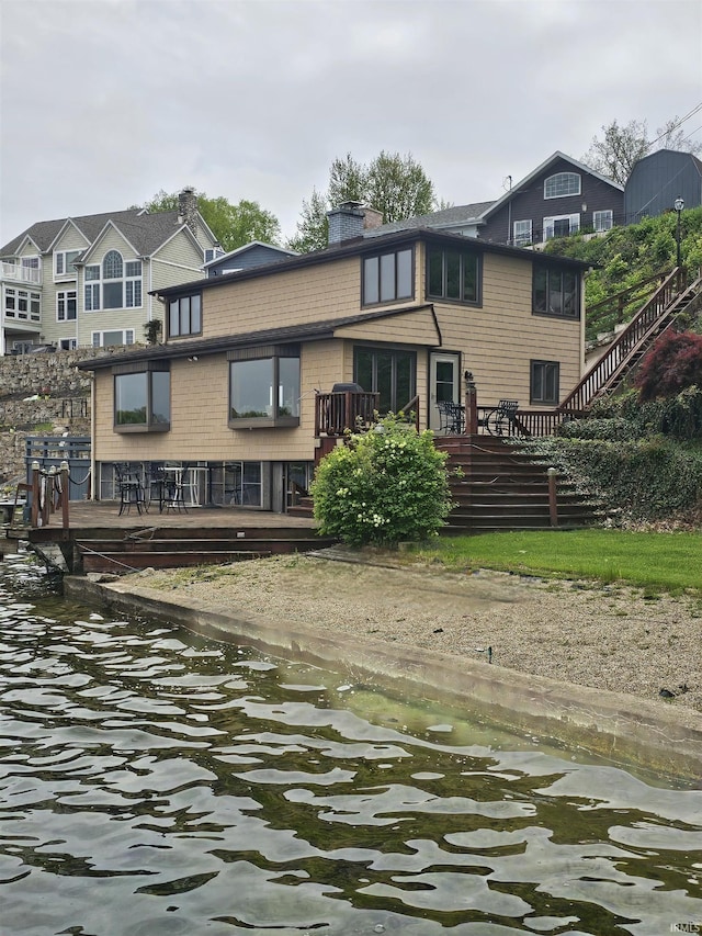 rear view of property with a deck with water view and a chimney