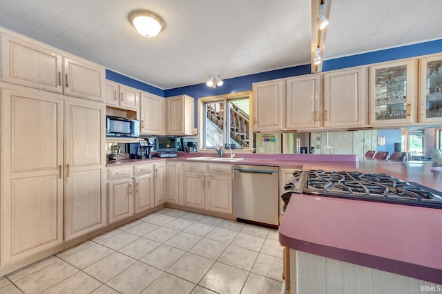 kitchen featuring dishwasher, a sink, light brown cabinetry, light tile patterned floors, and glass insert cabinets