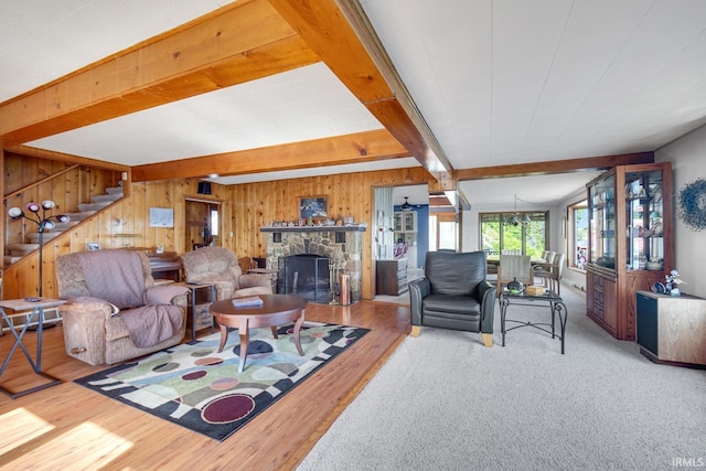 living area featuring beamed ceiling, wooden walls, a stone fireplace, wood finished floors, and stairs