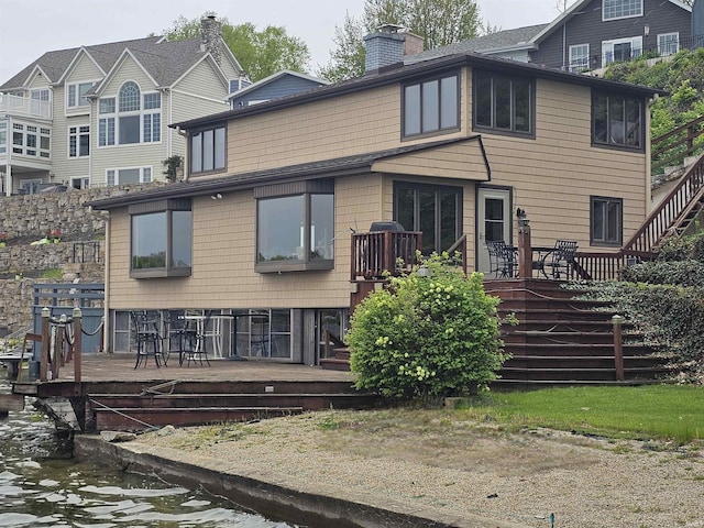 back of house with a deck with water view and a chimney