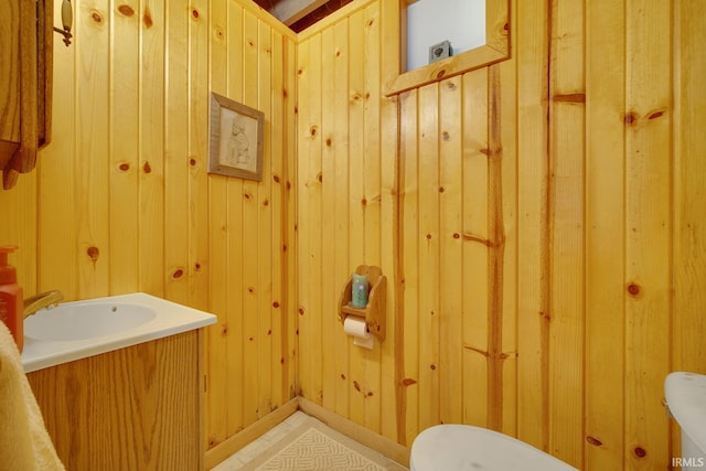 half bath featuring toilet, wood walls, and vanity