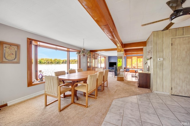 dining room featuring light colored carpet, a chandelier, wooden walls, a ceiling fan, and baseboards