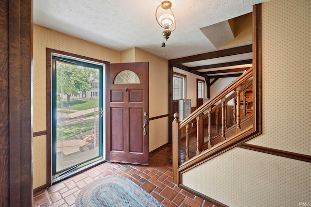 entryway featuring a textured ceiling, wallpapered walls, stairs, and brick floors