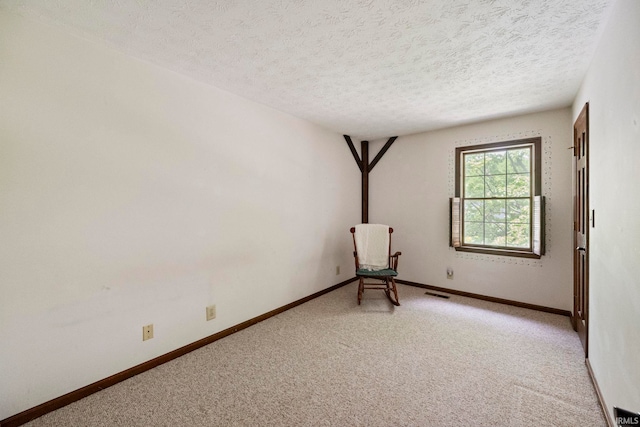 spare room featuring light colored carpet, a textured ceiling, and baseboards