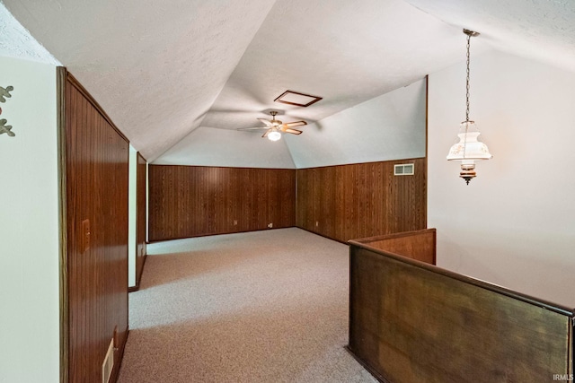 additional living space with wood walls, lofted ceiling, light carpet, and a textured ceiling