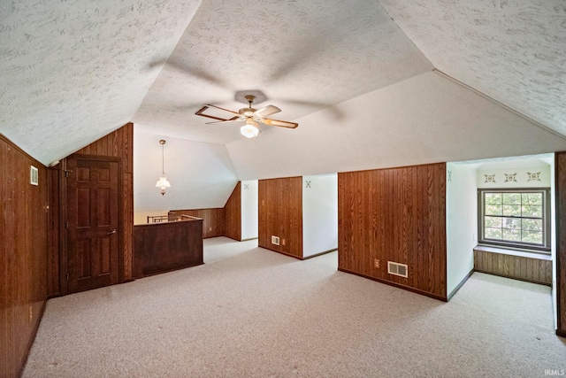 bonus room with wood walls, vaulted ceiling, a textured ceiling, light carpet, and a ceiling fan
