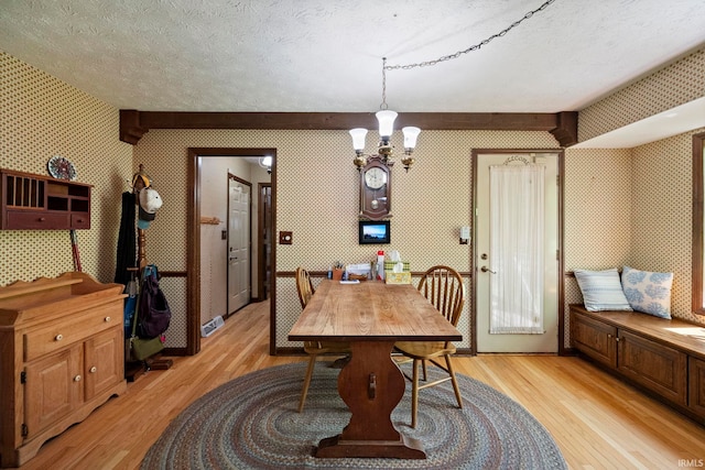 dining room featuring wallpapered walls, light wood-type flooring, a chandelier, and a textured ceiling