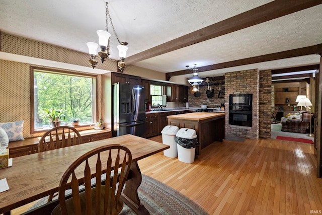 dining space with light wood-style flooring, a textured ceiling, a chandelier, and beam ceiling