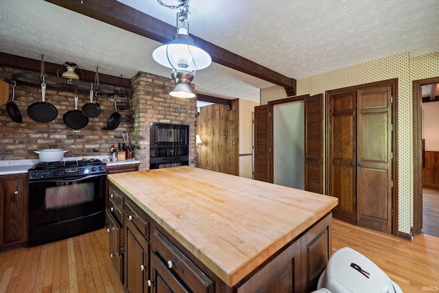 kitchen with black range with gas cooktop, butcher block countertops, light wood-style floors, beamed ceiling, and a textured ceiling