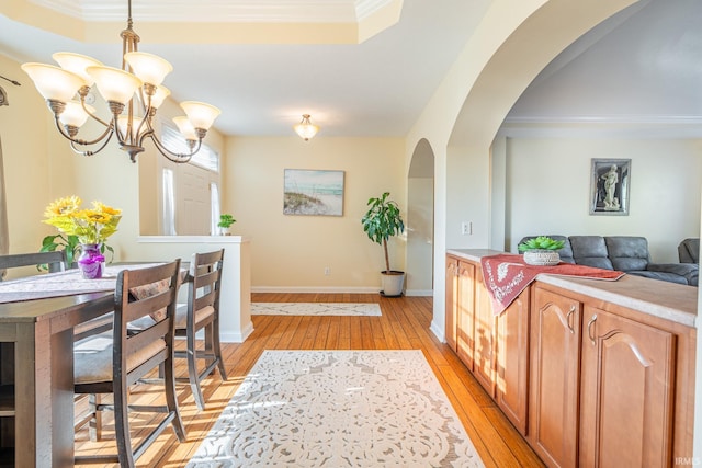 dining room with light wood-style flooring, arched walkways, crown molding, a chandelier, and baseboards