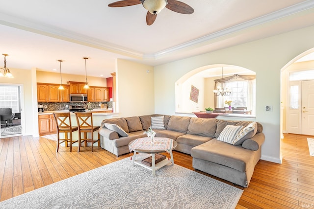 living area featuring arched walkways, light wood-type flooring, a chandelier, crown molding, and a ceiling fan