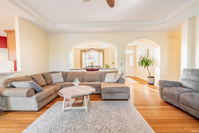 living room featuring a raised ceiling, arched walkways, light wood-type flooring, and ornamental molding