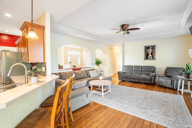 living area featuring a tray ceiling, a ceiling fan, light wood-type flooring, arched walkways, and recessed lighting