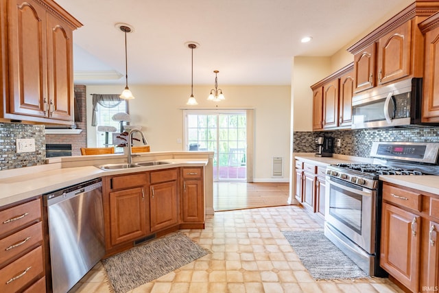 kitchen with stainless steel appliances, a sink, light countertops, decorative light fixtures, and brown cabinets