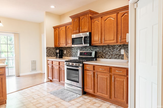 kitchen featuring appliances with stainless steel finishes, light flooring, light countertops, decorative backsplash, and brown cabinetry