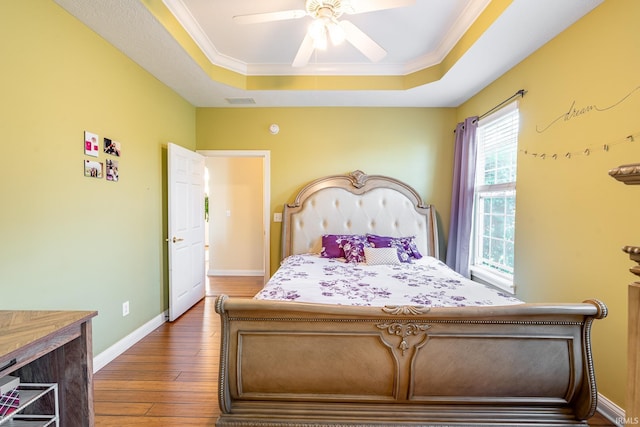 bedroom featuring a raised ceiling, hardwood / wood-style floors, baseboards, ornamental molding, and a ceiling fan