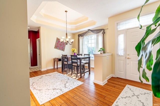 foyer entrance featuring a raised ceiling, a chandelier, hardwood / wood-style flooring, baseboards, and ornamental molding