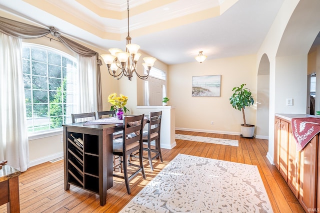 dining area with light wood finished floors, arched walkways, a chandelier, a raised ceiling, and baseboards