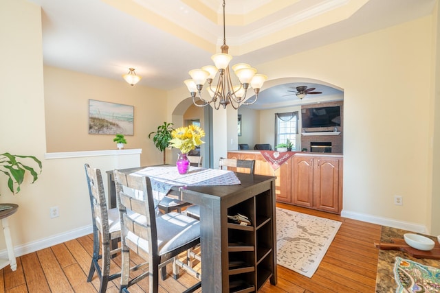 dining area with arched walkways, light wood finished floors, a raised ceiling, a ceiling fan, and a chandelier