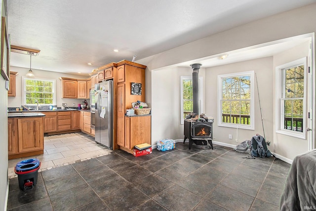 kitchen with stainless steel fridge with ice dispenser, a wood stove, dark countertops, baseboards, and recessed lighting